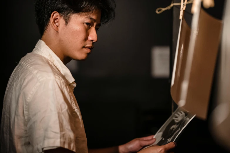 a close up of a person holding a cell phone, a charcoal drawing, inspired by Yamagata Hiro, unsplash, hyperrealism, stands at a his easel, asian man, x-ray photography, side profile portrait