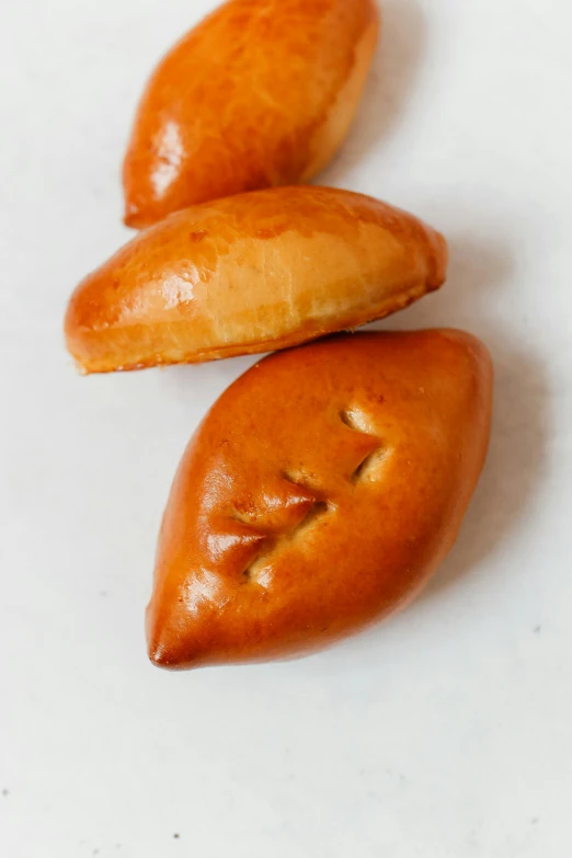 three pieces of bread sitting on top of a white surface, inspired by Slava Raškaj, hurufiyya, with a pointed chin, moroccan, smooth oval shape face, pastries