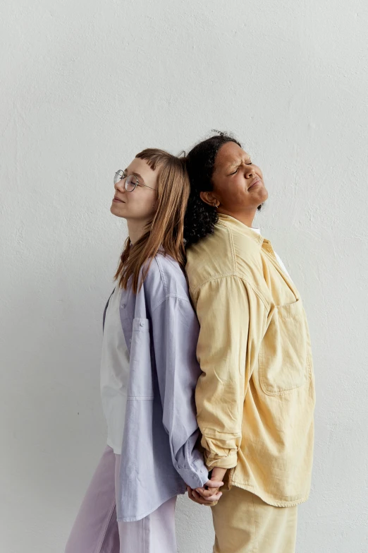 a man and a woman standing next to each other, trending on pexels, yellow purple, lesbian, long shirt, mixed race