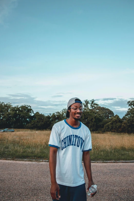 a man standing in the middle of a road, an album cover, trending on unsplash, brown skin man with a giant grin, wearing a backwards baseball cap, blue skies, clement hurd