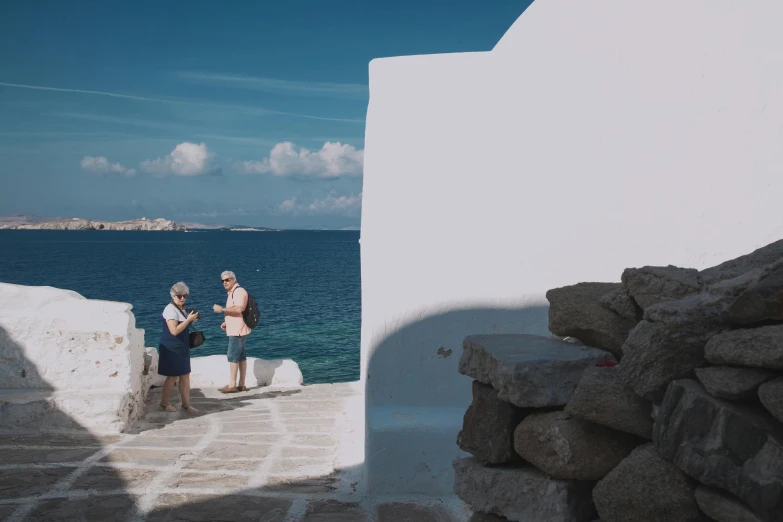 a couple of people standing next to a body of water, by Alexis Grimou, greek architecture, background image, slide show, cinematic footage