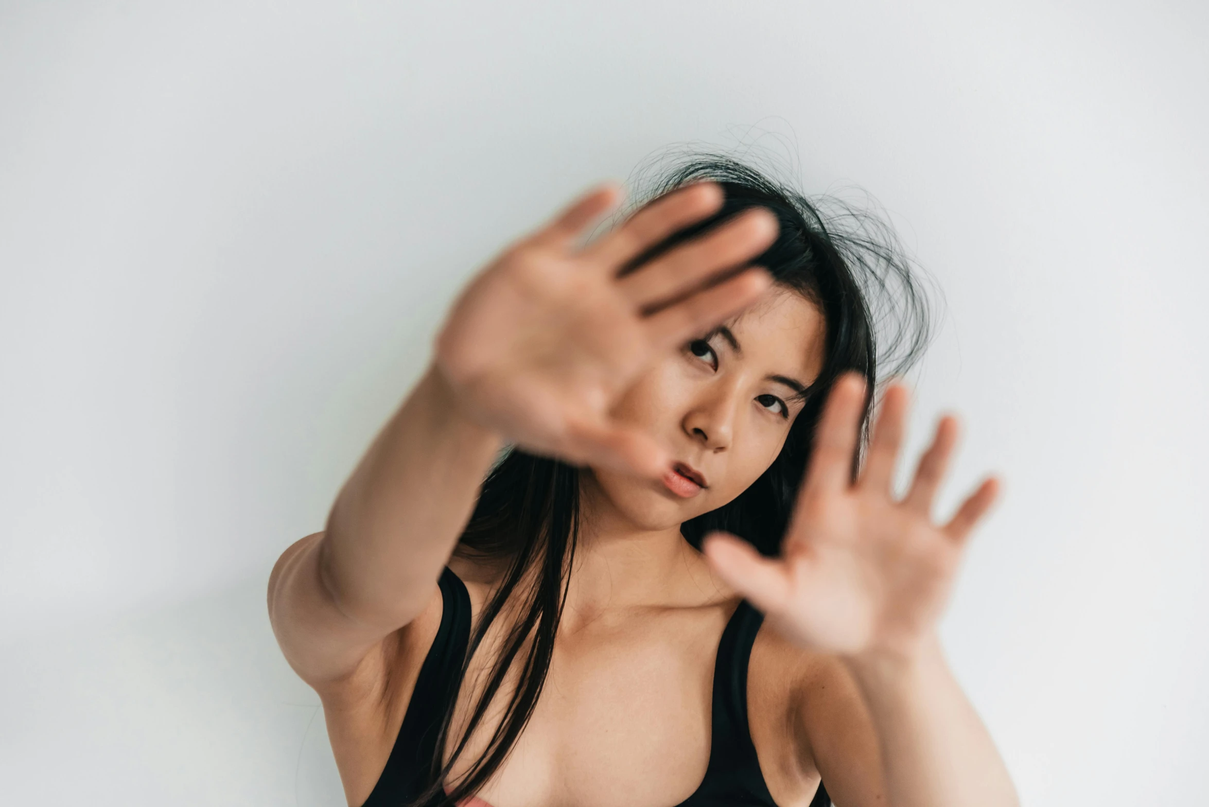 a woman making a stop sign with her hands, trending on pexels, visual art, asian face, she is wearing a black tank top, scratches on photo, woman with porcelain skin