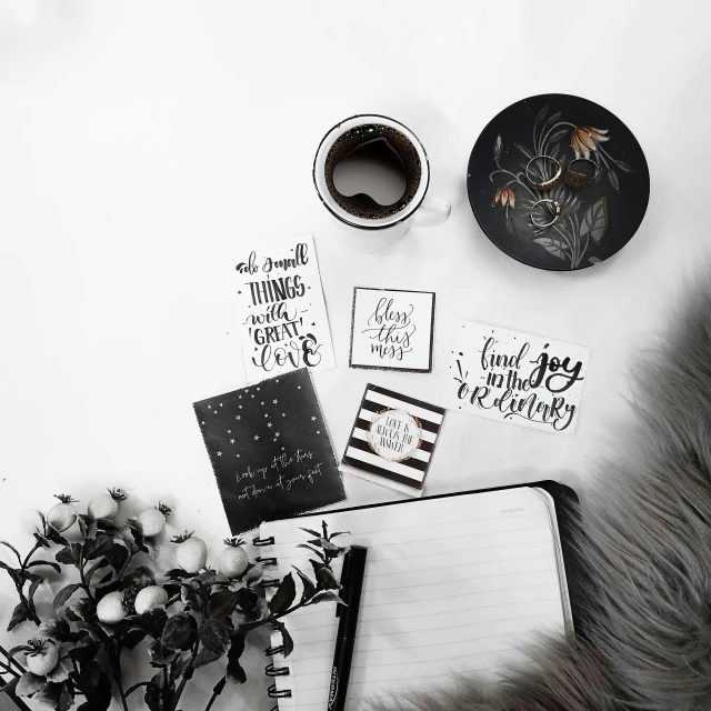 a table topped with a notebook and a cup of coffee, a black and white photo, planner stickers, all black matte product, illustration », saying