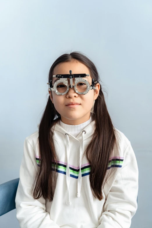 a little girl sitting on top of a blue chair, with navigator shaped glasses, wearing a lab coat, inuit, detailed pupils