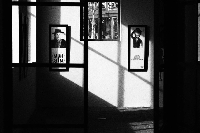 a black and white photo of posters on a wall, a poster, inspired by Brassaï, purism, sunlight through windows, noir detective and a fedora, shot with iphone 1 0, portrait!!!!