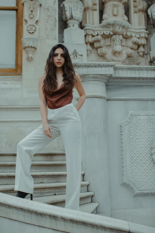 a woman standing on the steps of a building, inspired by Elsa Bleda, trending on pexels, renaissance, white pants, young woman with long dark hair, dressed in silk, portait image