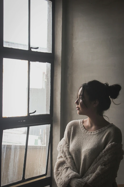 a woman sitting in front of a window, inspired by Elsa Bleda, pexels contest winner, wearing a white sweater, korean woman, sad man, low quality photo