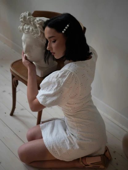 a woman sitting on a chair next to a statue, inspired by Konstantin Somov, unsplash, wearing a wet white short dress, hands in her hair. side-view, product introduction photo, puff sleeves