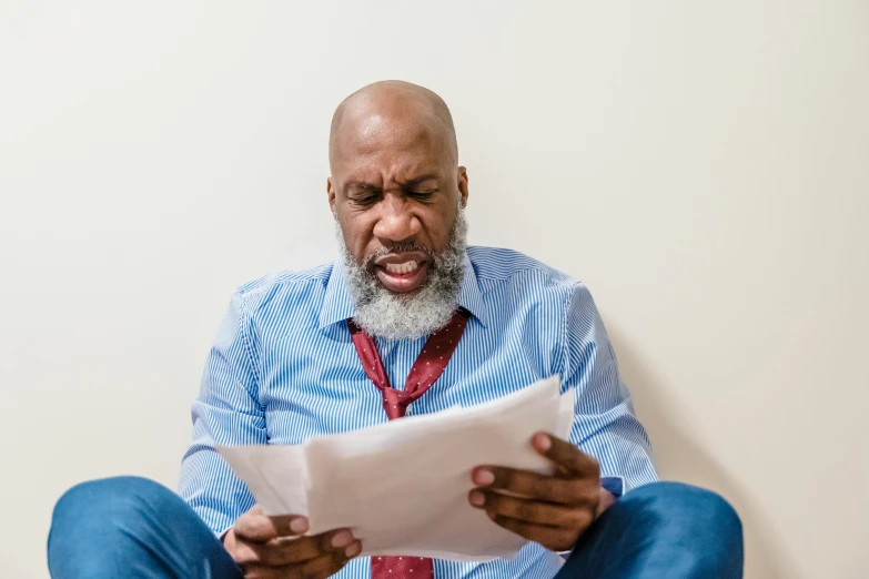 a man sitting on the floor reading a piece of paper, mc ride, some grey hair in beard, stressful, document photo