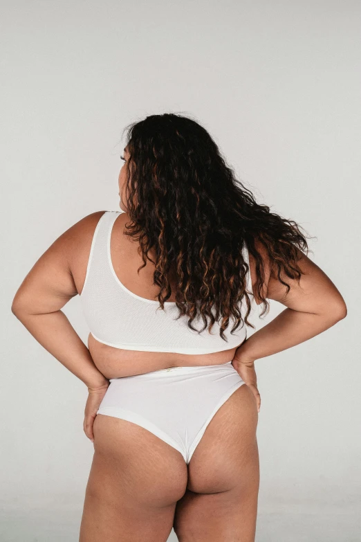 a woman in a white underwear posing for a picture, facing away from the camera, plus-sized, back view »