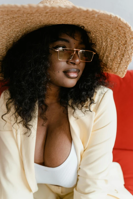 a woman sitting on a red couch wearing a straw hat, trending on pexels, sexy girl with dark complexion, square rimmed glasses, breasts covered and sfw, sza