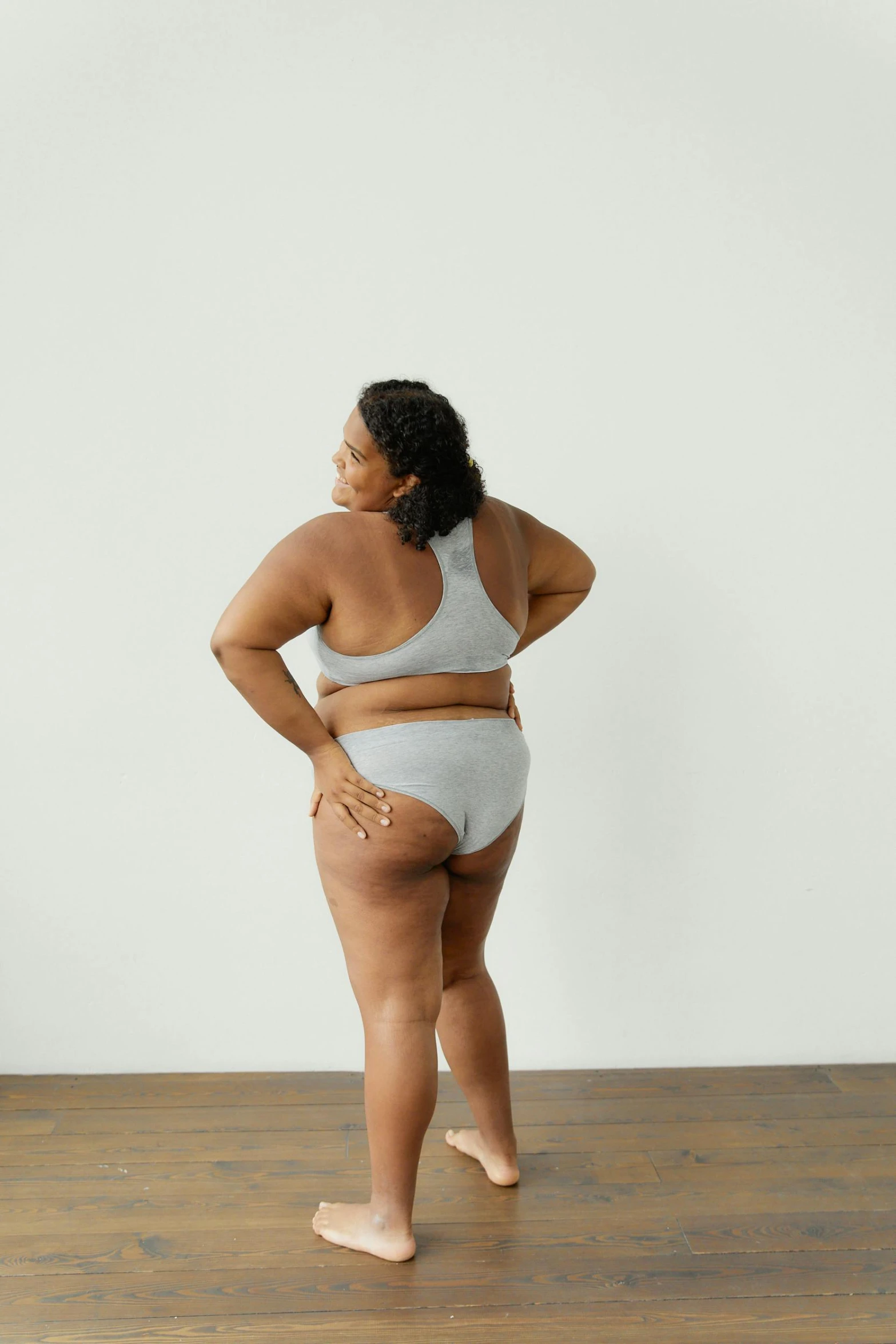 a woman standing on top of a wooden floor, by Emily Shanks, shaped derriere, light grey, lizzo, on grey background