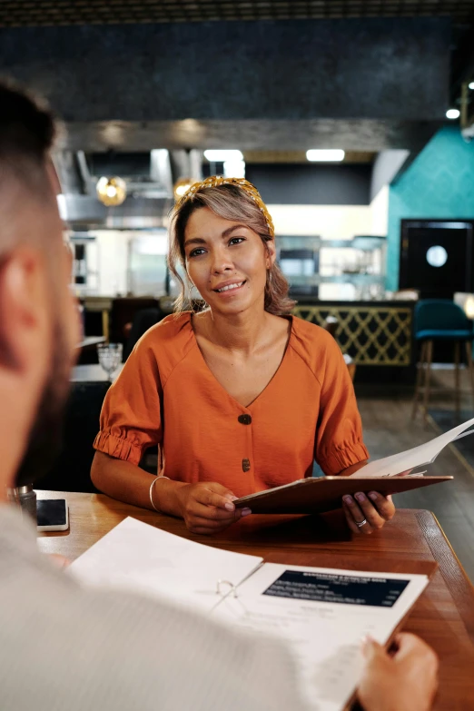 a man and woman sitting at a table in a restaurant, holding a clipboard, giving an interview, high-quality photo, thumbnail