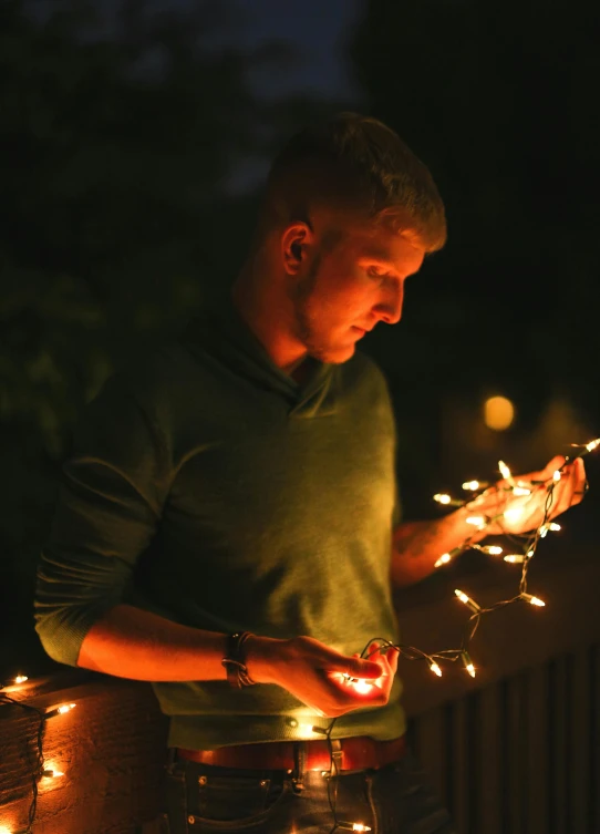 a man standing next to a fence holding a string of lights, profile image, sparklers, multiple stories, holiday season