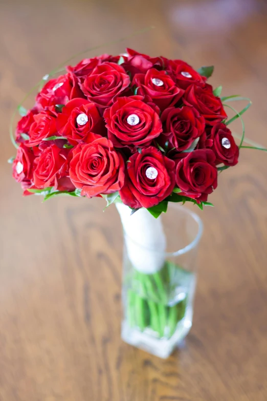 a vase filled with red roses on top of a wooden table, inspired by Alfred Jensen, with sparkling gems on top, highly no detailed, bouquet, displayed