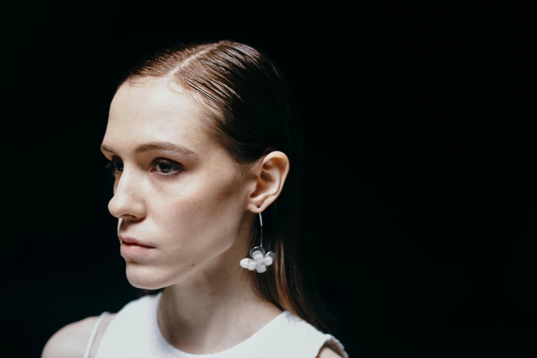 a woman standing in front of a black background, by Nina Hamnett, unsplash, earrings, fashion week backstage, slight bloom, off - white collection