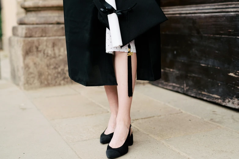 a woman wearing a black coat and a white dress, trending on pexels, talons, wearing an academic gown, rachel walpole, illegible