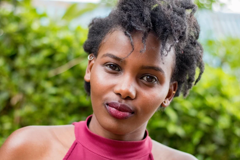 a close up of a person wearing a pink top, by Lily Delissa Joseph, pexels contest winner, hurufiyya, natural hair, very kenyan, high cheekbones, cheeky smile with red lips