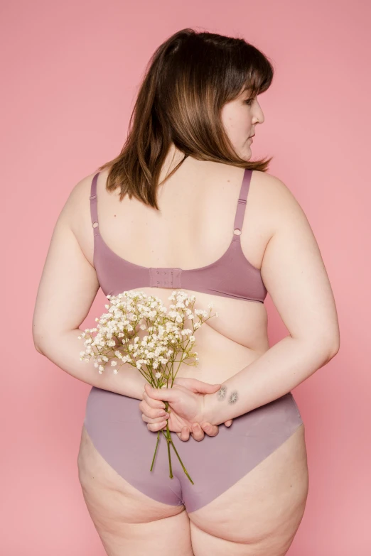 a woman in underwear holding a bouquet of flowers, a colorized photo, unsplash, mauve background, an obese, back arched, wearing bra