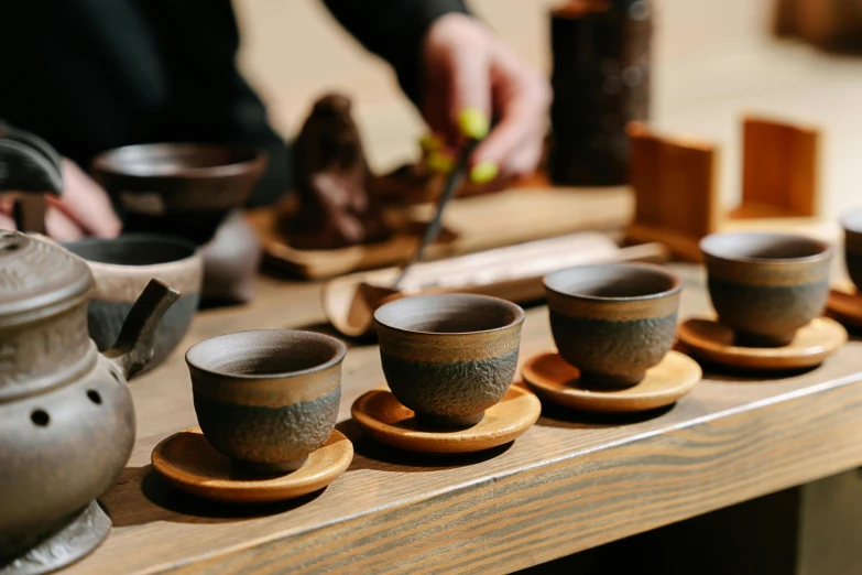 a close up of cups and saucers on a table, inspired by Kanō Shōsenin, trending on unsplash, mingei, made of tar, working in the forge, in style of lam manh, brown