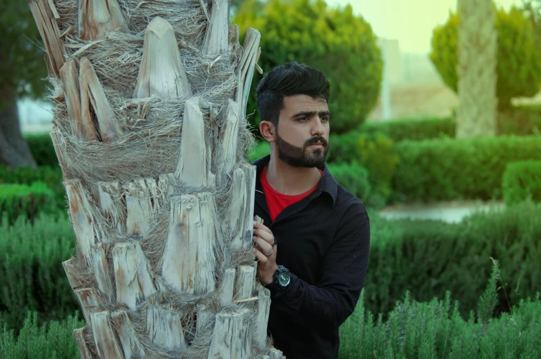 a man standing next to a palm tree, a picture, by Ismail Acar, pexels contest winner, realism, assyrian, casual pose, avatar image, handsome