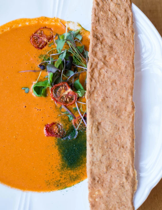 a white plate topped with a bowl of soup next to a piece of bread, inspired by Géza Dósa, unsplash, process art, paprika, panorama, also one tomato slice, medium close up shot