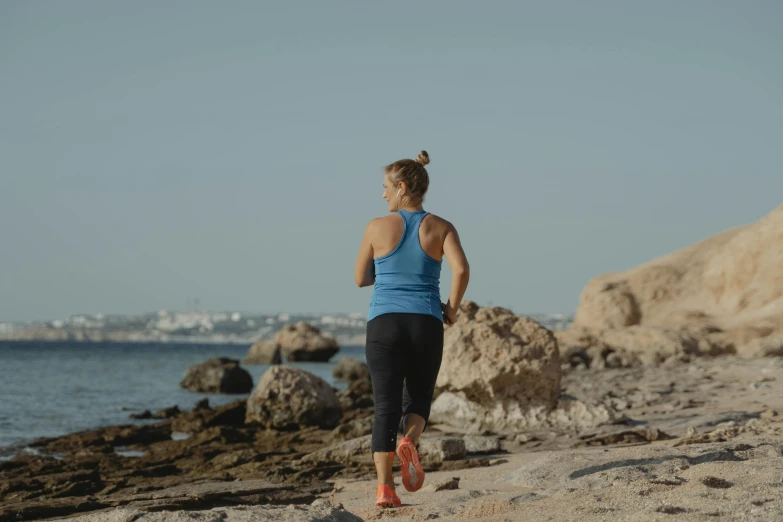 a woman running on a beach next to the ocean, profile image, costa blanca, standing on rocky ground, avatar image