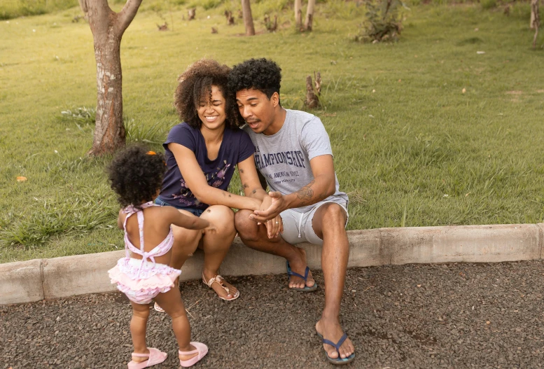 a man and woman sitting next to a little girl, by Paul Davis, pexels, happening, curly afro, parks, hill, husband wife and son