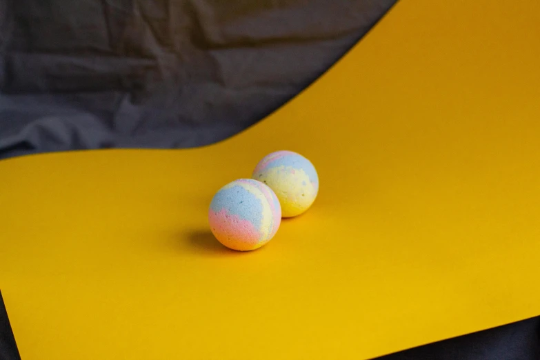 a couple of eggs sitting on top of a yellow table, inspired by Pearl Frush, unsplash, process art, blue and pink colour splash, marshmallows, muted rainbow tubing, sweet night ambient