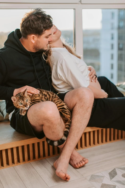 a man and a woman sitting on a window sill with a cat, by Julia Pishtar, pexels contest winner, kissing together cutely, tigers, relaxing on a modern couch, manuka