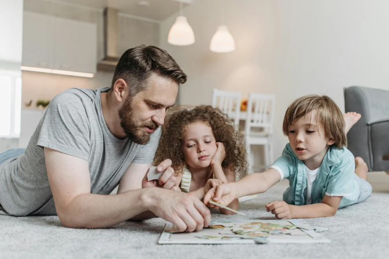 a man and two small children laying on the floor, a jigsaw puzzle, by Adam Marczyński, pexels contest winner, board games on a table, avatar image