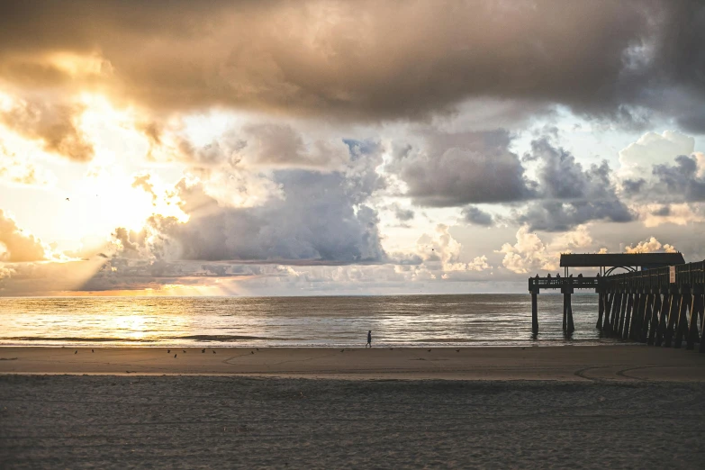 a person standing on a beach under a cloudy sky, boardwalk, golden hour photograph, photograph