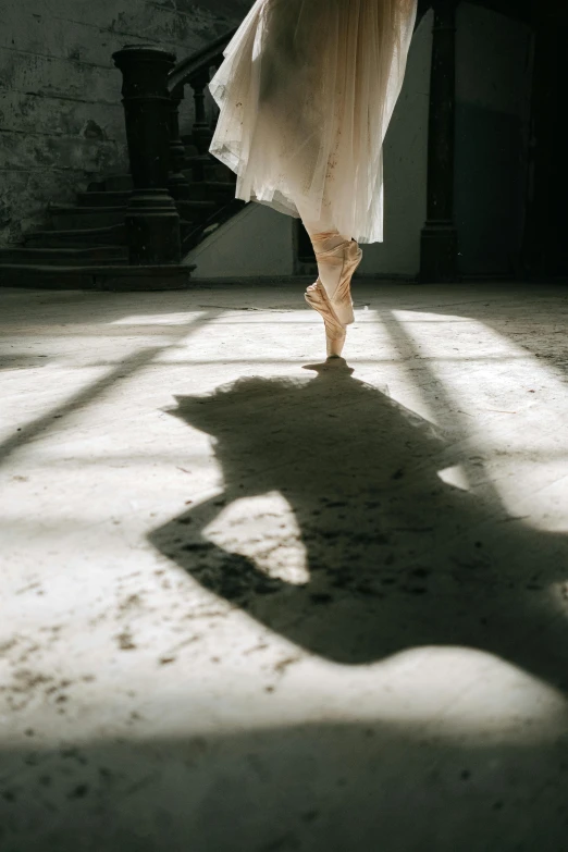 a woman in a white dress is dancing, by Elizabeth Polunin, unsplash contest winner, arabesque, long cast shadows, morning light showing injuries, ( ( theatrical ) ), dusty floor