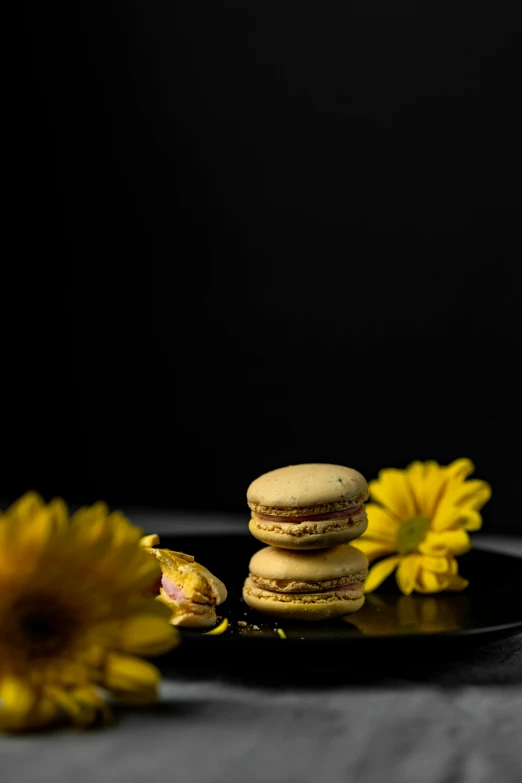 a black plate topped with macarons next to yellow flowers, a portrait, unsplash, medium format. soft light, portrait n - 9, made of food, with a black background