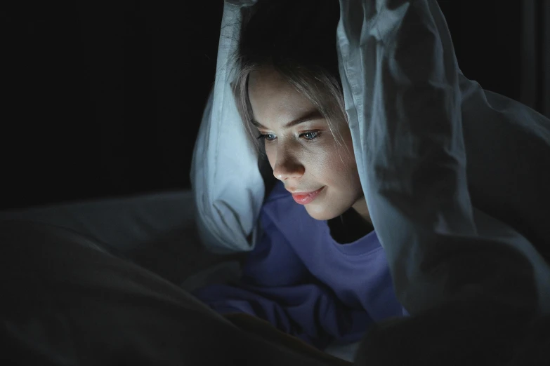a woman laying in bed looking at a cell phone, by Adam Marczyński, hurufiyya, emerging from her lamp, wearing a dark hood, 18 years old, glow up