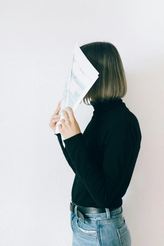 a woman holding a piece of paper in front of her face, pexels contest winner, black turtle neck shirt, in front of white back drop, profile image, faceless