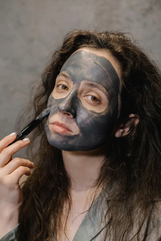 a woman is putting a mask on her face, inspired by Marina Abramović, charcoal color skin, thumbnail, skincare, slate