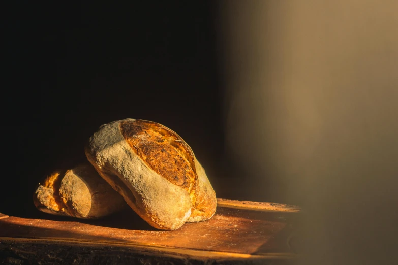 a loaf of bread sitting on top of a wooden cutting board, a portrait, unsplash, hyperrealism, beams of golden light, woodfired, ignant, traditional corsican