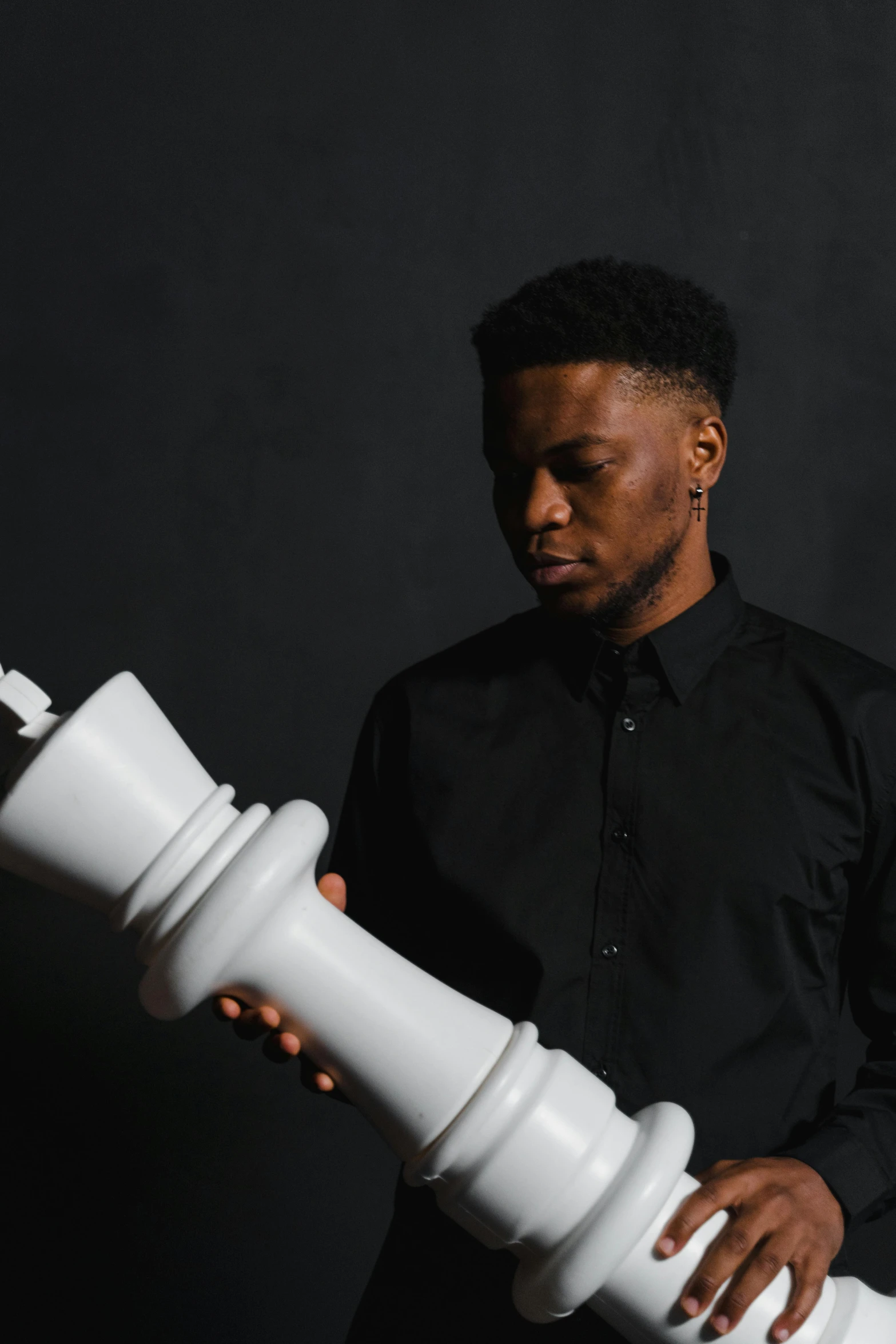 a man holding a giant white chess piece, an album cover, inspired by Xanthus Russell Smith, pexels contest winner, realism, black velvet, side profile portrait, plain background, instagram picture