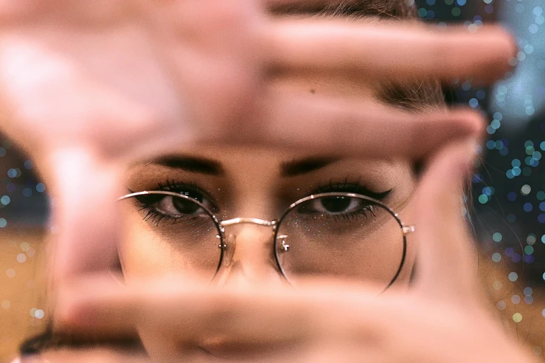 a woman wearing glasses making a frame with her hands, a picture, by Adam Marczyński, trending on pexels, seductive eyes, multiple perspectives, sparkle in eyes, spying