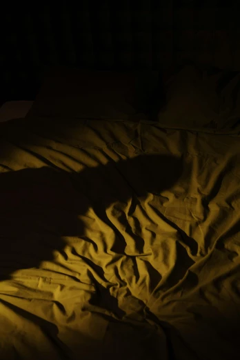 a person laying on a bed in the dark, yellow light, dark shadow, un made bed, photographed for reuters