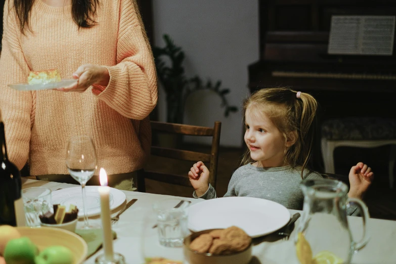 a little girl sitting at a table with a plate of food, holding a candle, with a kid, being delighted and cheerful, abcdefghijklmnopqrstuvwxyz