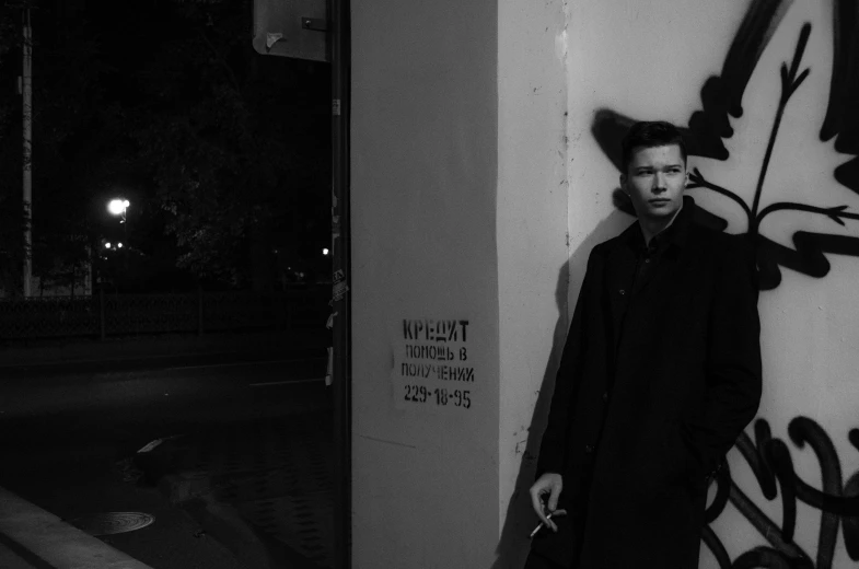 a man standing next to a wall with graffiti on it, a black and white photo, by Emma Andijewska, tumblr, bauhaus, julian ope, in the evening, maxim sukharev, promotional image