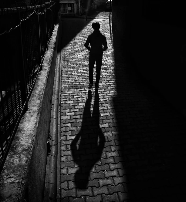 a black and white photo of a person walking down a street, by Daniel Gelon, pexels contest winner, deep shadows and colors, sergey krasovskiy, light over boy, high shadow