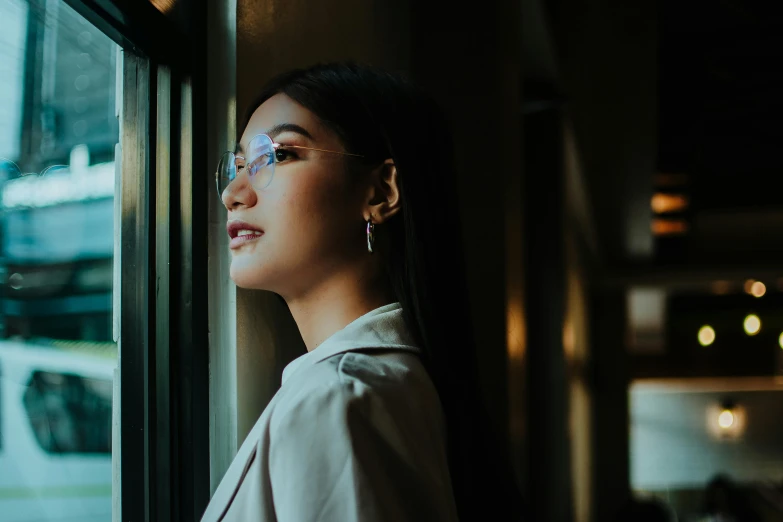 a woman is looking out of a window, inspired by Ruth Jên, trending on pexels, wearing square glasses, beautiful asian woman, thoughtful ), good lighted photo