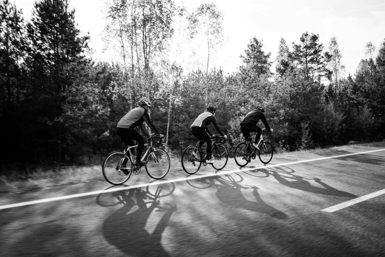 a group of bicyclists riding down a road, a black and white photo, by Kristian Zahrtmann, unsplash, espoo, nike cycling suit, trio, spinning