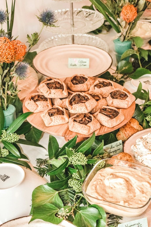 a table topped with plates of food and flowers, by Dulah Marie Evans, in the shape of a cinnamon roll, lush greenery, celebration of coffee products, closeup - view