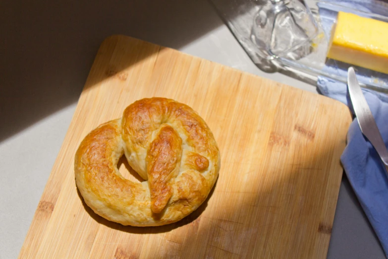 a pretzel sitting on top of a wooden cutting board, inspired by Richmond Barthé, featured on reddit, hurufiyya, sun overhead, pastry lizard, white, lightweight