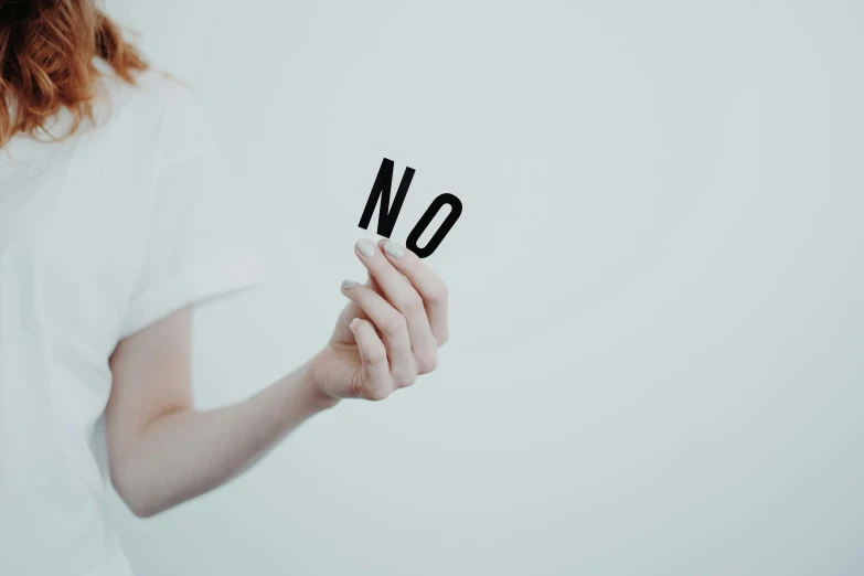 a woman holding up a sign that says no, by Arabella Rankin, unsplash, minimalist sticker, studio shoot, unfocused, two