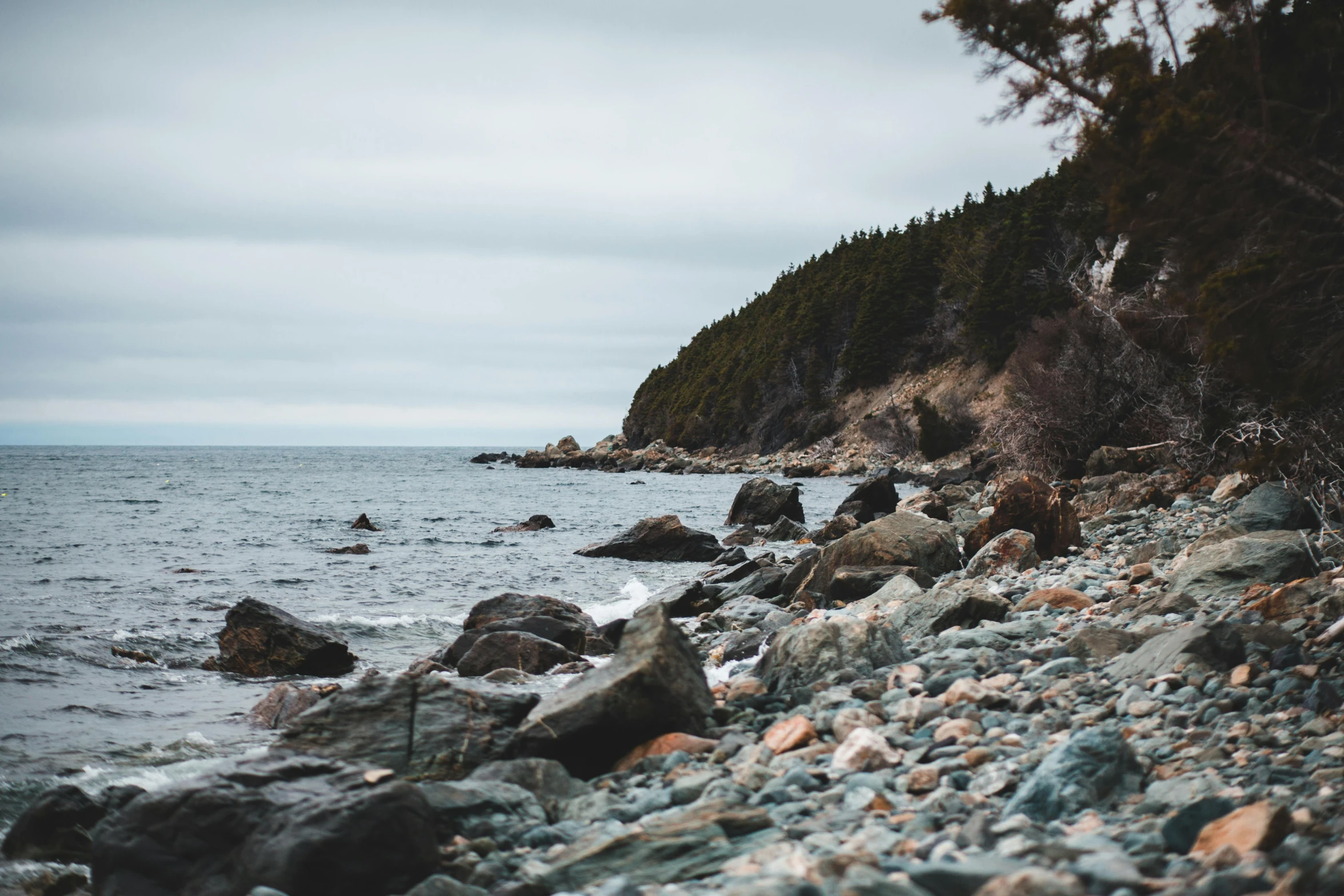 a rocky beach next to a body of water, unsplash, visual art, quebec, 2 5 6 x 2 5 6 pixels, ((rocks)), hills and ocean